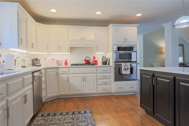 kitchen featuring white cabinets, decorative light fixtures, stainless steel appliances, and light hardwood / wood-style flooring