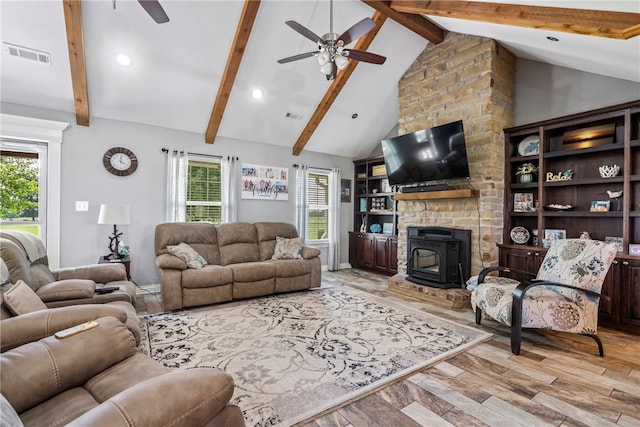 living room featuring beamed ceiling, a stone fireplace, light hardwood / wood-style flooring, and ceiling fan