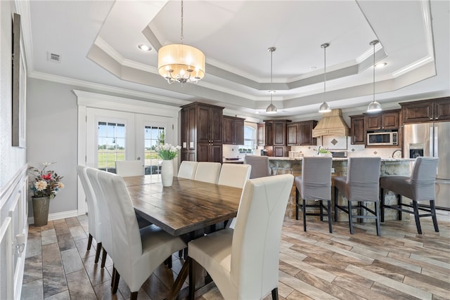 dining space with ornamental molding, a notable chandelier, french doors, and a raised ceiling