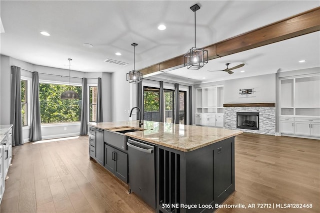 kitchen with dishwasher, pendant lighting, a center island with sink, and light stone countertops