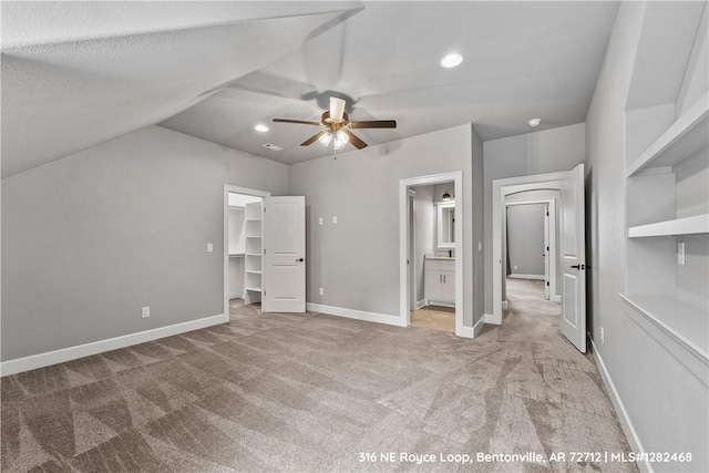 unfurnished bedroom with a walk in closet, ceiling fan, connected bathroom, a closet, and lofted ceiling