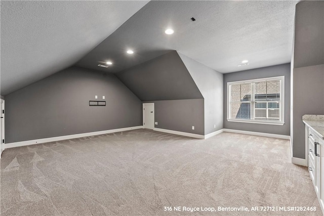 bonus room featuring a textured ceiling, light colored carpet, and vaulted ceiling