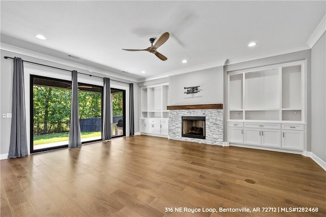 unfurnished living room featuring ornamental molding, ceiling fan, built in features, light hardwood / wood-style flooring, and a stone fireplace