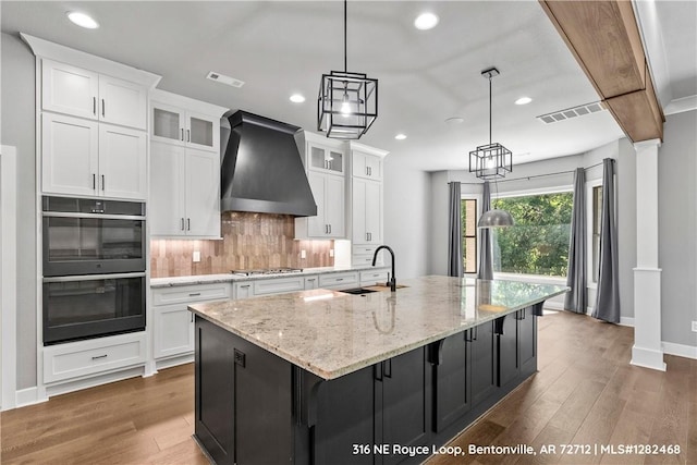 kitchen featuring backsplash, a spacious island, sink, custom range hood, and white cabinetry