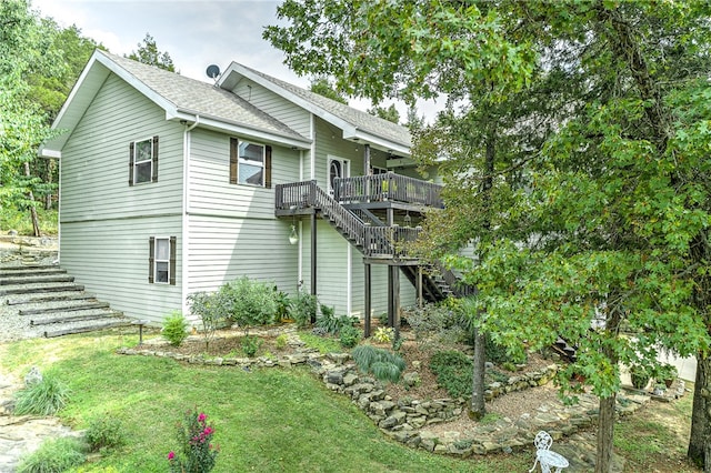 view of side of home with stairway, a yard, a wooden deck, and a shingled roof