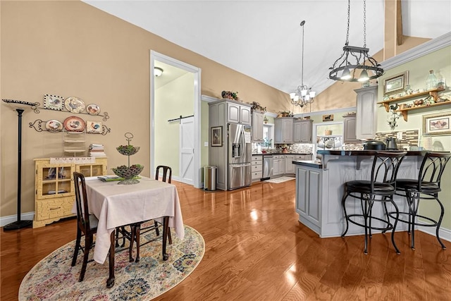 kitchen with gray cabinetry, kitchen peninsula, stainless steel appliances, a barn door, and decorative backsplash