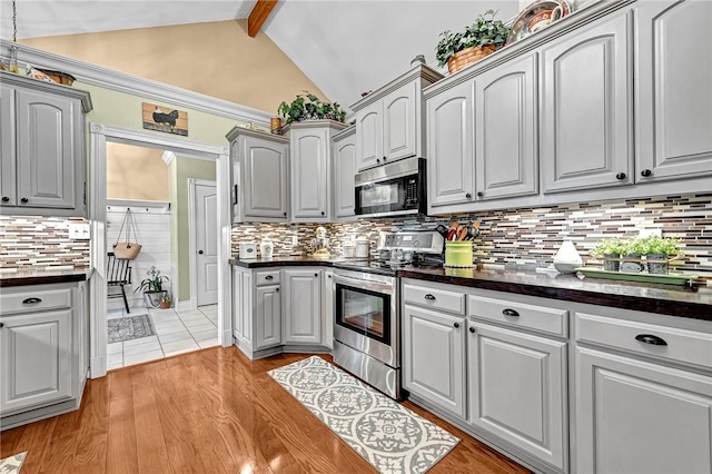 kitchen with stainless steel appliances, gray cabinetry, backsplash, and lofted ceiling with beams