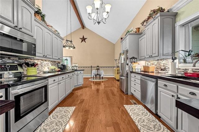 kitchen with appliances with stainless steel finishes, gray cabinetry, hanging light fixtures, an inviting chandelier, and light hardwood / wood-style flooring