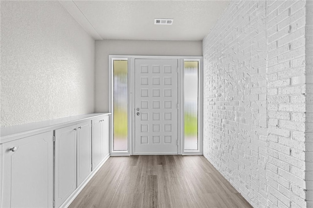 foyer entrance with brick wall, a textured ceiling, and light hardwood / wood-style flooring