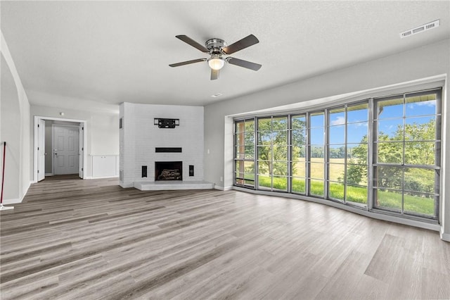 unfurnished living room with a brick fireplace, hardwood / wood-style floors, a textured ceiling, and ceiling fan