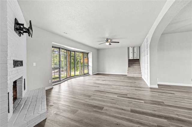 unfurnished living room with a brick fireplace, hardwood / wood-style floors, a textured ceiling, and ceiling fan