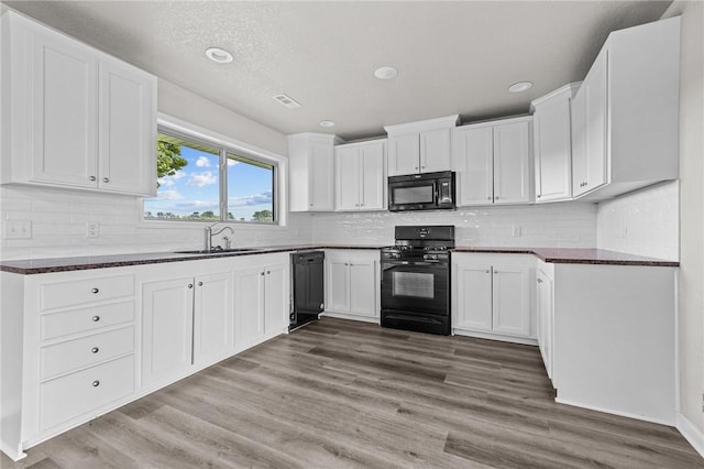 kitchen with tasteful backsplash, wood-type flooring, sink, white cabinets, and black appliances