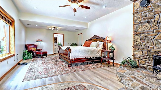 bedroom featuring a textured ceiling, wood finished floors, visible vents, baseboards, and a wood stove