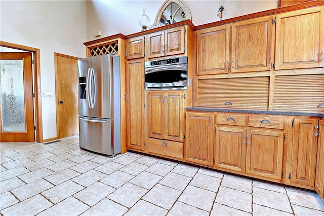 kitchen featuring light tile patterned floors, brown cabinetry, dark countertops, a towering ceiling, and appliances with stainless steel finishes