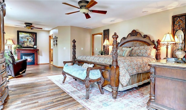 bedroom with a ceiling fan, a glass covered fireplace, baseboards, and wood finished floors