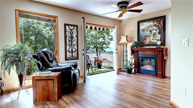 living area featuring a glass covered fireplace, ceiling fan, baseboards, and wood finished floors