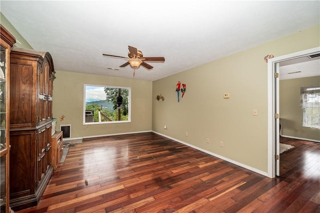 unfurnished room featuring a ceiling fan, baseboards, dark wood finished floors, and a wealth of natural light