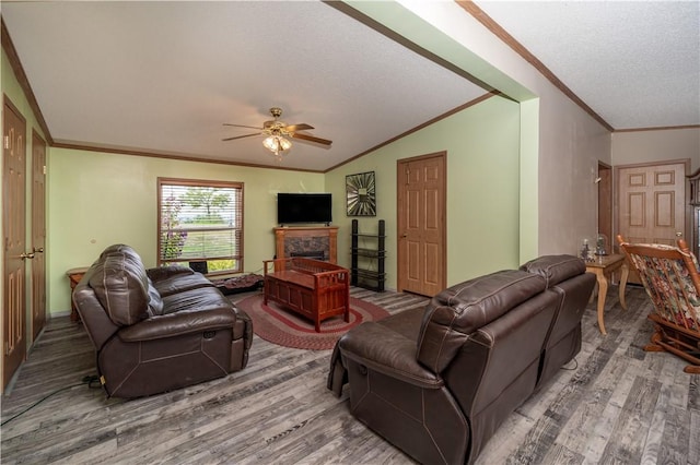 living area with ceiling fan, lofted ceiling, a fireplace, wood finished floors, and crown molding