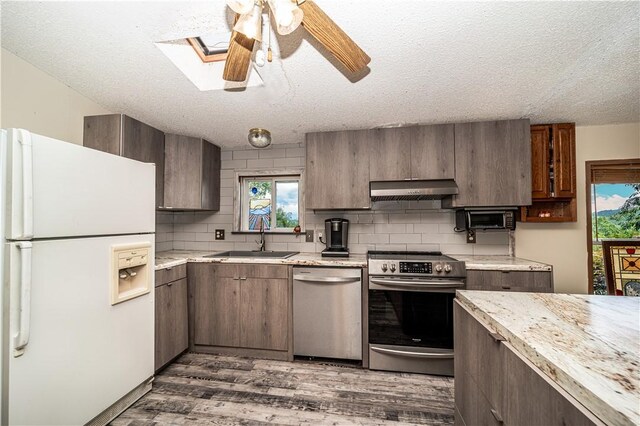 kitchen featuring a skylight, ceiling fan, stainless steel appliances, hardwood / wood-style floors, and sink