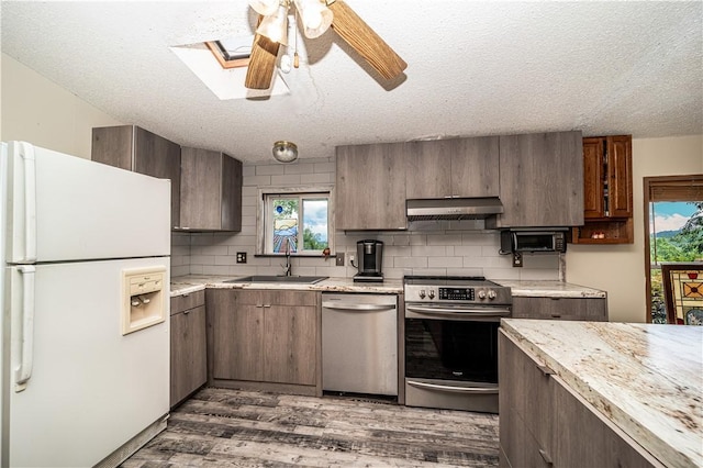 kitchen featuring decorative backsplash, appliances with stainless steel finishes, light countertops, under cabinet range hood, and a sink