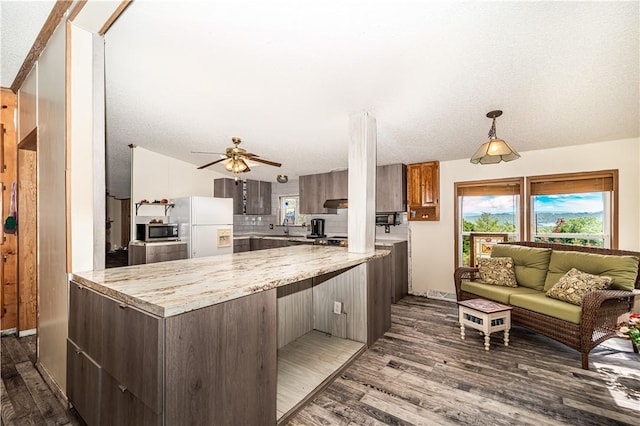 kitchen with white fridge with ice dispenser, stainless steel microwave, a peninsula, and light countertops