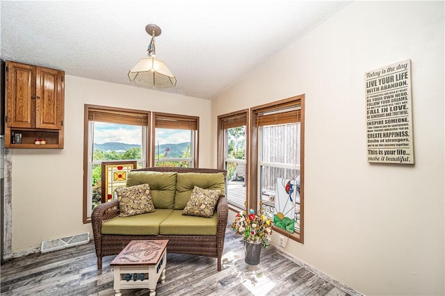 living area with lofted ceiling, visible vents, a textured ceiling, wood finished floors, and baseboards