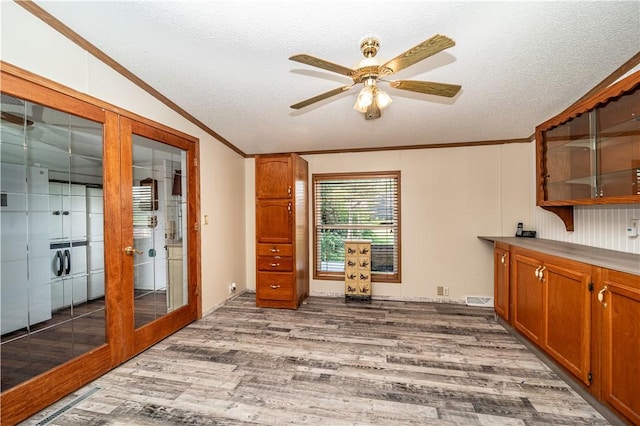 interior space with french doors, lofted ceiling, ornamental molding, a textured ceiling, and wood finished floors