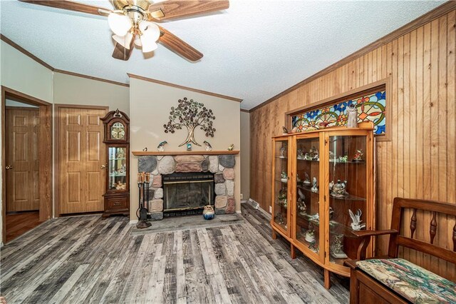 sitting room featuring wooden walls, hardwood / wood-style flooring, a fireplace, a textured ceiling, and ceiling fan