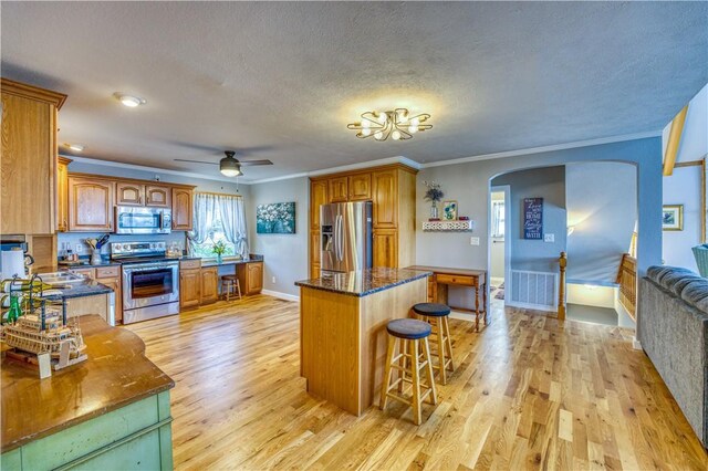 kitchen featuring a center island, stainless steel appliances, light wood-type flooring, and crown molding