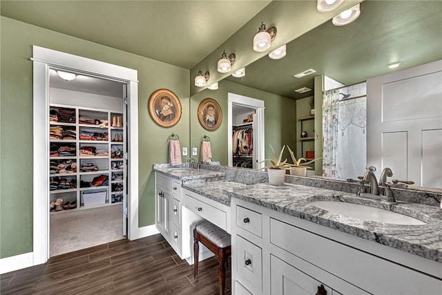 bathroom with wood finished floors, double vanity, a spacious closet, curtained shower, and baseboards