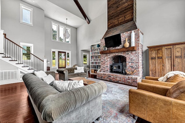 living room featuring a high ceiling, wood-type flooring, stairs, a wood stove, and beamed ceiling