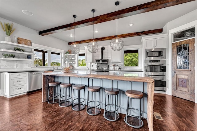 kitchen featuring stainless steel appliances, backsplash, a kitchen breakfast bar, white cabinets, and a center island with sink
