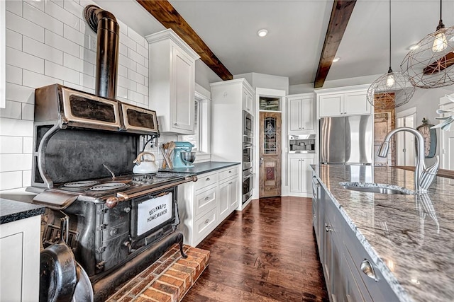 kitchen featuring stainless steel appliances, a sink, beamed ceiling, dark wood finished floors, and dark stone countertops