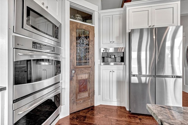kitchen with stainless steel appliances, stone countertops, white cabinets, and dark wood-style floors