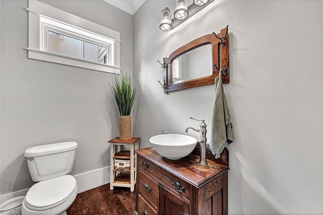 half bath with toilet, wood finished floors, and vanity