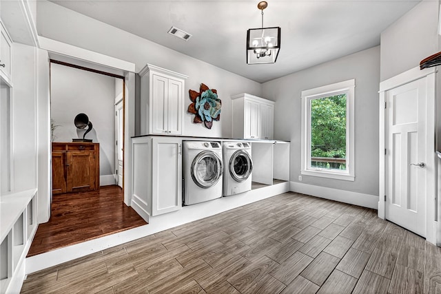 washroom with a notable chandelier, washing machine and dryer, hardwood / wood-style floors, and cabinets