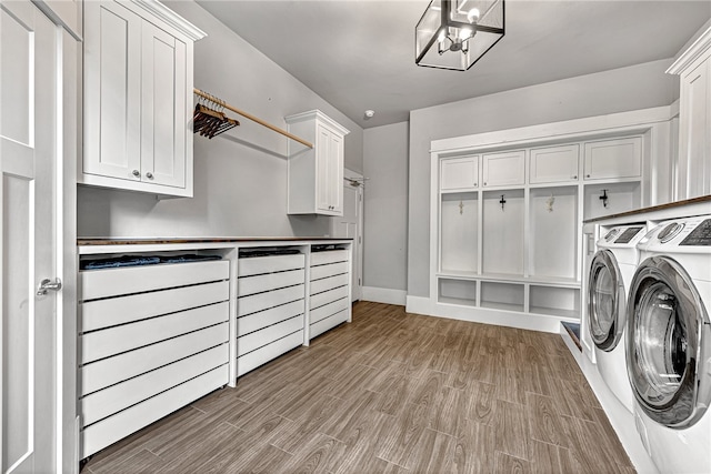 clothes washing area featuring washer and clothes dryer, a chandelier, cabinets, and light hardwood / wood-style floors