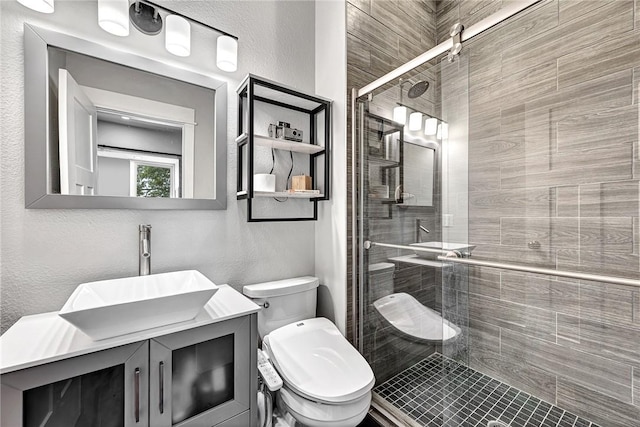 bathroom featuring a stall shower, toilet, vanity, and a textured wall