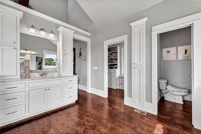 bathroom with toilet, wood finished floors, vanity, baseboards, and a walk in closet