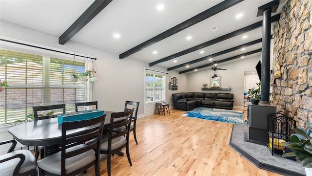 dining area featuring a wood stove, light hardwood / wood-style flooring, and vaulted ceiling with beams