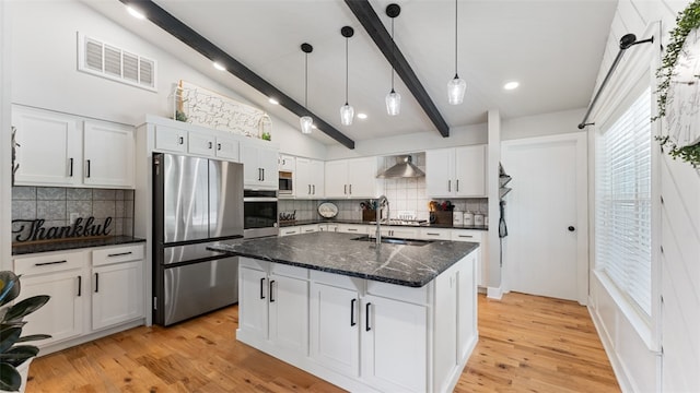 kitchen featuring vaulted ceiling with beams, appliances with stainless steel finishes, decorative backsplash, light wood-type flooring, and a kitchen island with sink