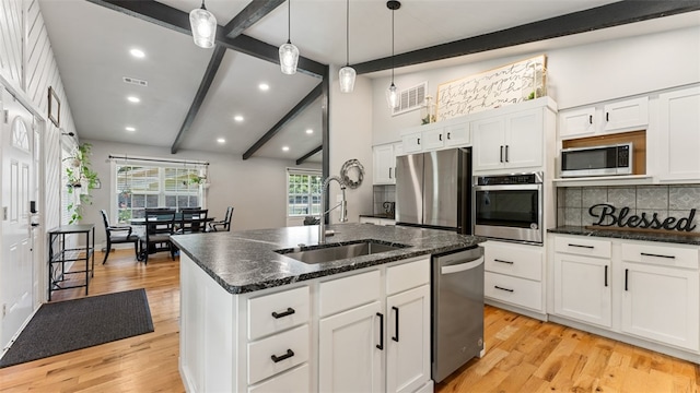 kitchen with stainless steel appliances, sink, light hardwood / wood-style flooring, backsplash, and a kitchen island with sink