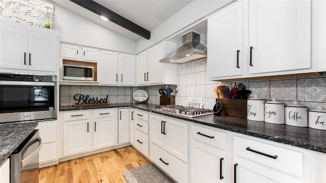 kitchen with wall chimney range hood, light hardwood / wood-style floors, appliances with stainless steel finishes, decorative backsplash, and lofted ceiling with beams