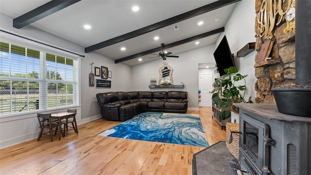 living room featuring a wood stove, lofted ceiling with beams, light wood-type flooring, and ceiling fan