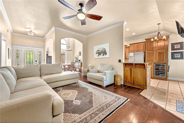 living room with a textured ceiling, wine cooler, ceiling fan with notable chandelier, hardwood / wood-style flooring, and ornamental molding