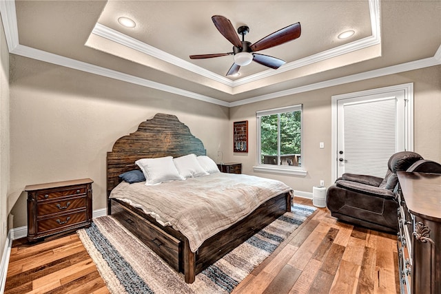 bedroom featuring ornamental molding, ceiling fan, light wood-type flooring, and a tray ceiling