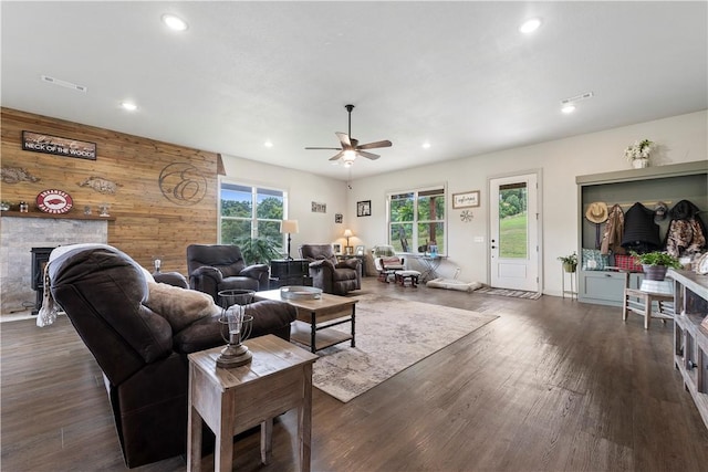 living room featuring ceiling fan, wood walls, a stone fireplace, and dark hardwood / wood-style floors