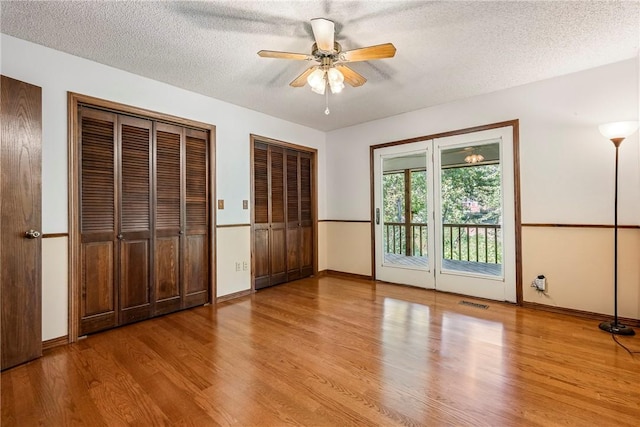 unfurnished bedroom featuring ceiling fan, access to exterior, a textured ceiling, light hardwood / wood-style floors, and multiple closets