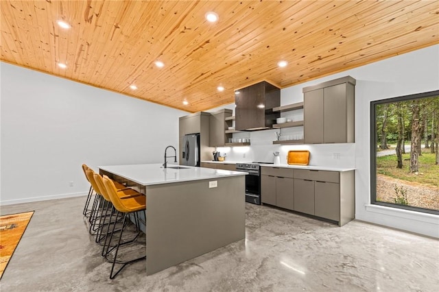 kitchen featuring wall chimney range hood, gray cabinets, a breakfast bar, appliances with stainless steel finishes, and a center island with sink