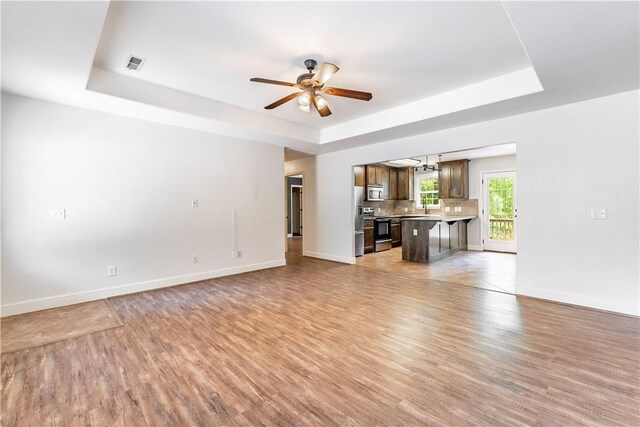 unfurnished living room featuring ceiling fan, light tile patterned flooring, and a tray ceiling